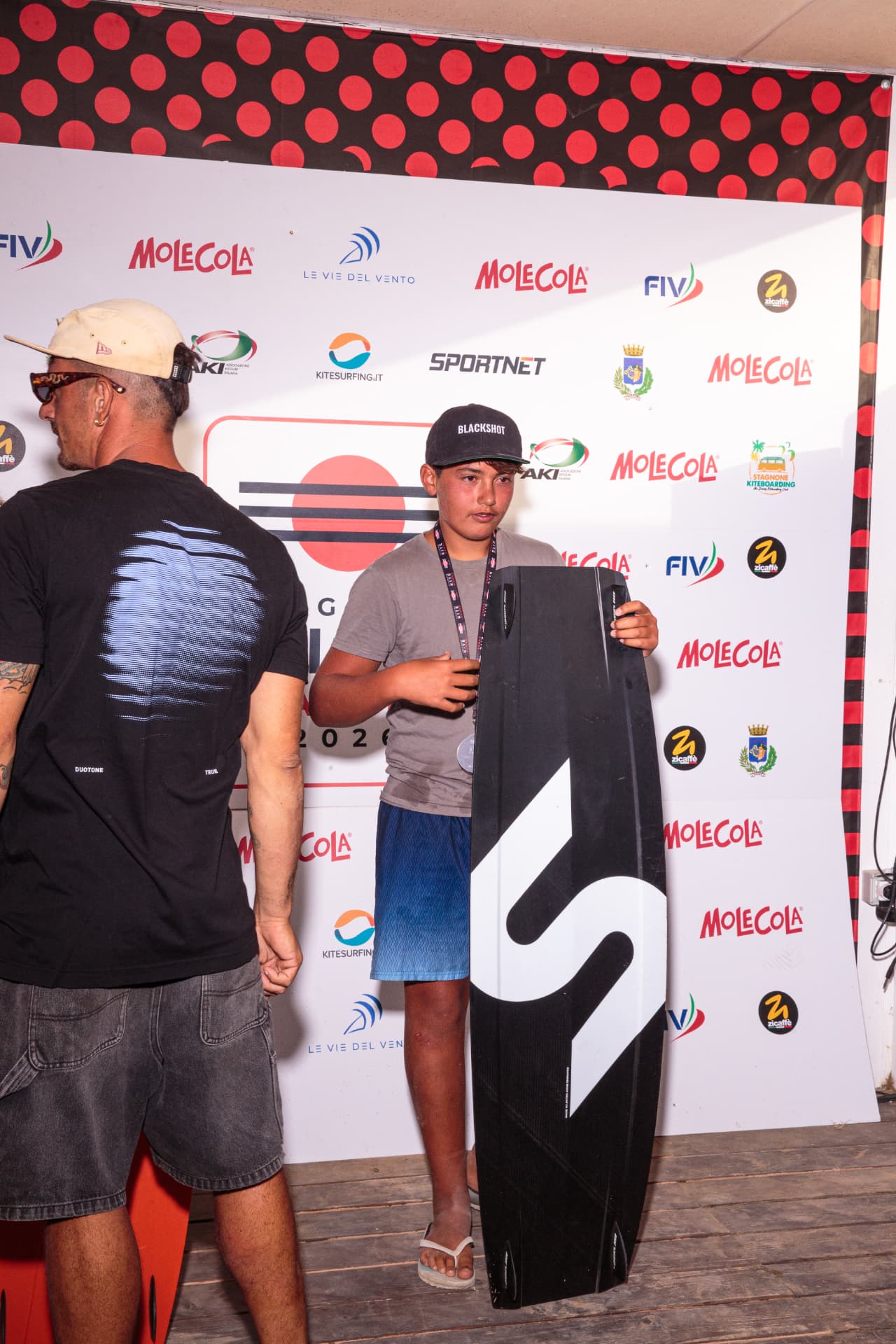Atleta con tavola premio e medaglia d'argento davanti al backdrop 2026